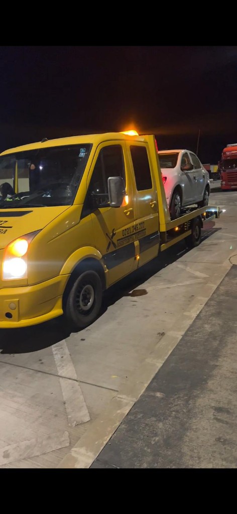 Platformă de tractare galbenă cu autoturism încărcat, noaptea.