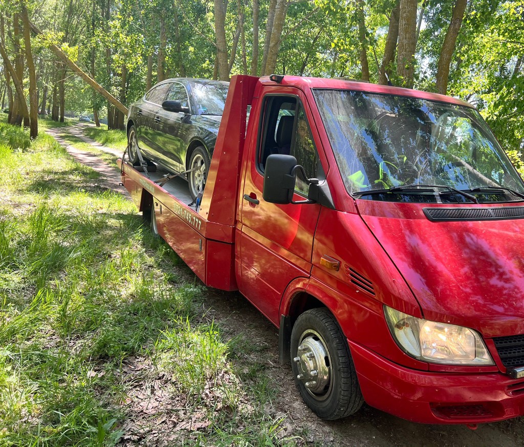 Platformă de tractare pe un drum de acces, cu autoturism încărcat.
